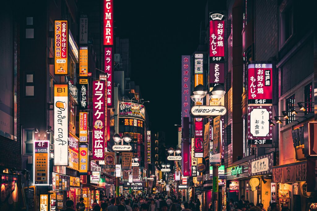 Night view of a busy Tokyo street with vibrant neon signs and people walking in Shinjuku, Japan.