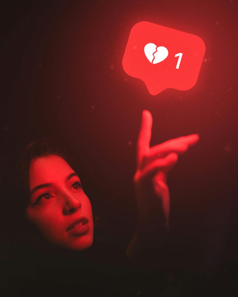 Red-hued image of a woman reaching towards a broken heart icon symbolizing digital detachment.