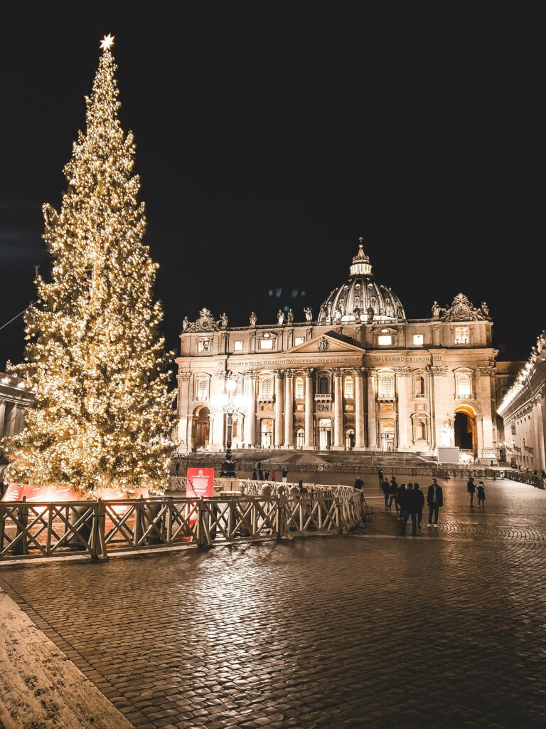 Illuminated St. Peter's Basilica and Christmas tree at night in Vatican City, showcasing festive holiday spirit.