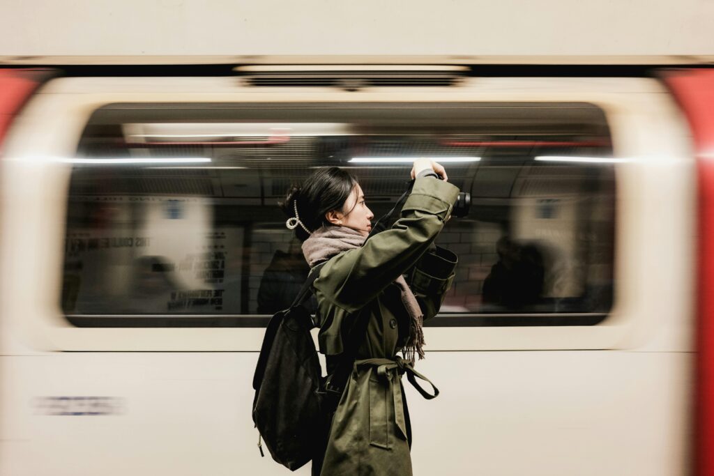 Woman photographing moving London Underground train, capturing motion blur and urban life.