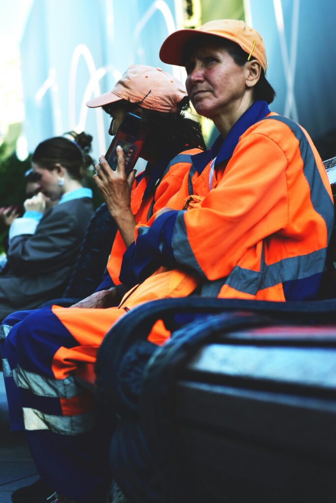 Two urban workers in reflective uniforms take a break on a bench reflecting city life.