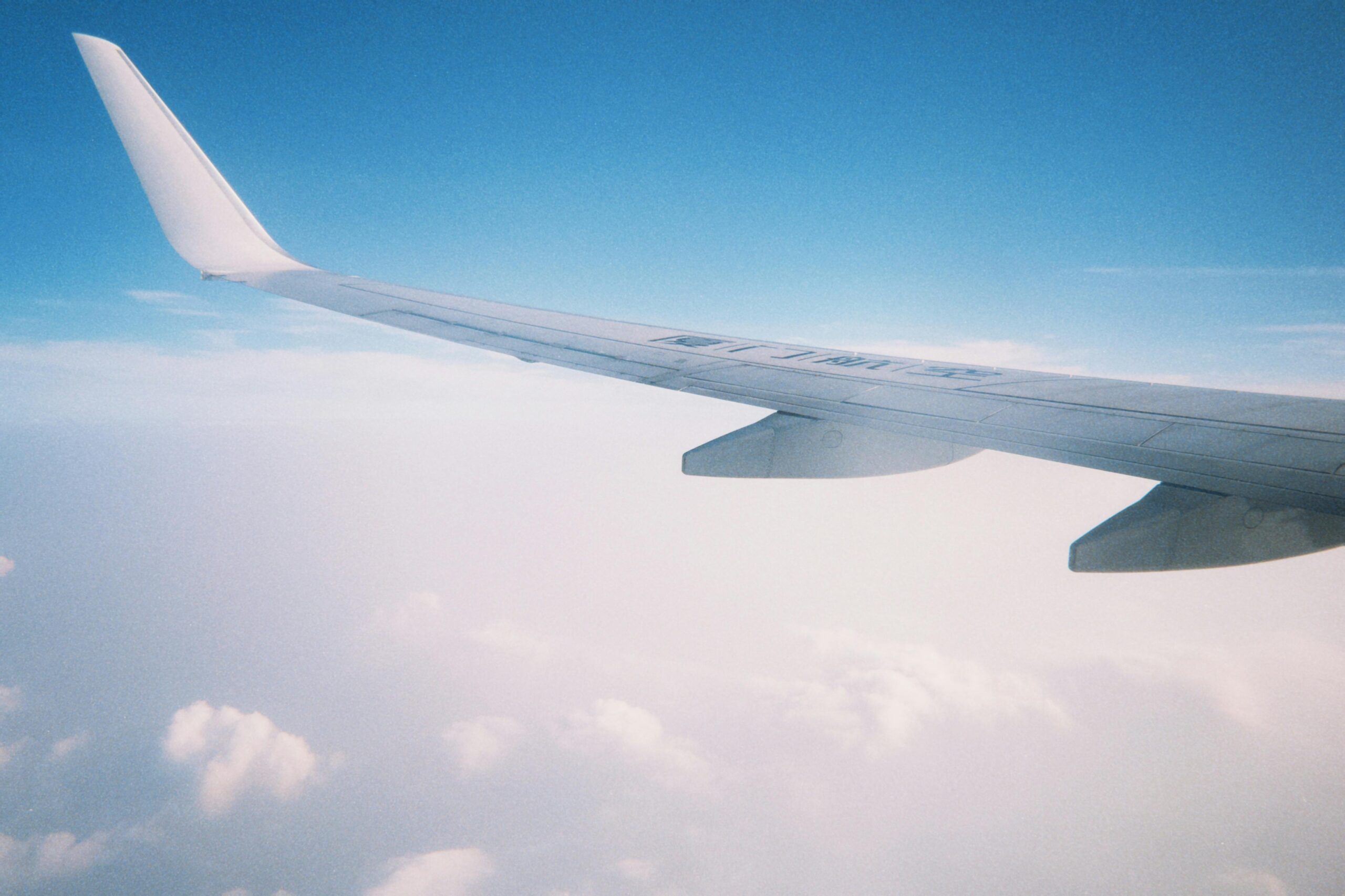 View of airplane wing gliding above clouds against a clear blue sky.