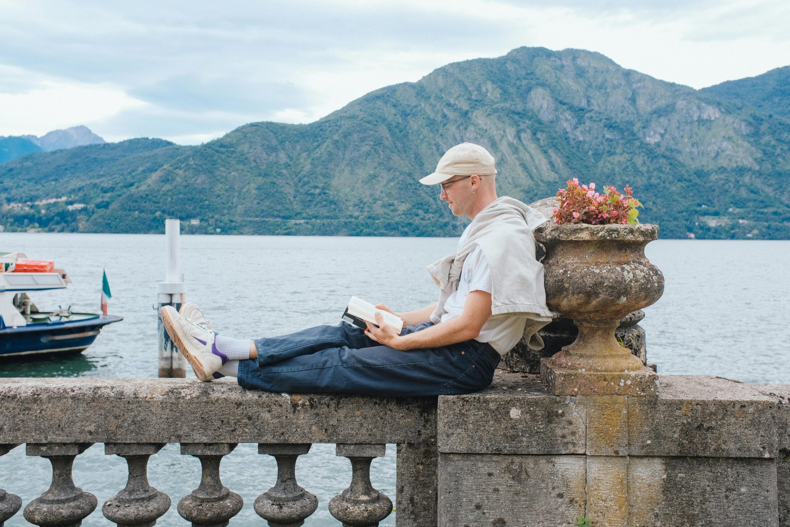 A man relaxing and reading a book by the lakeside with mountain backdrop.