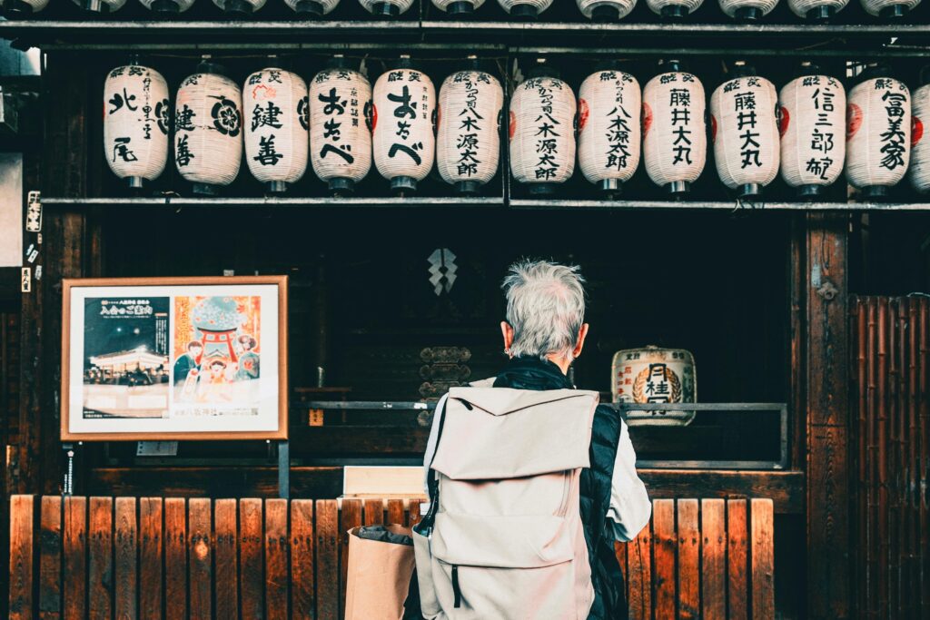 Back view of traveler with backpack looking at hanging Japanese lanterns outdoors.