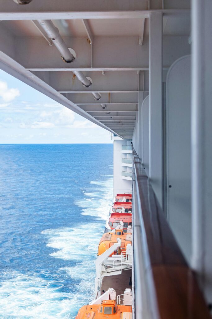 Side view of a cruise ship at sea with open ocean and lifeboats visible.