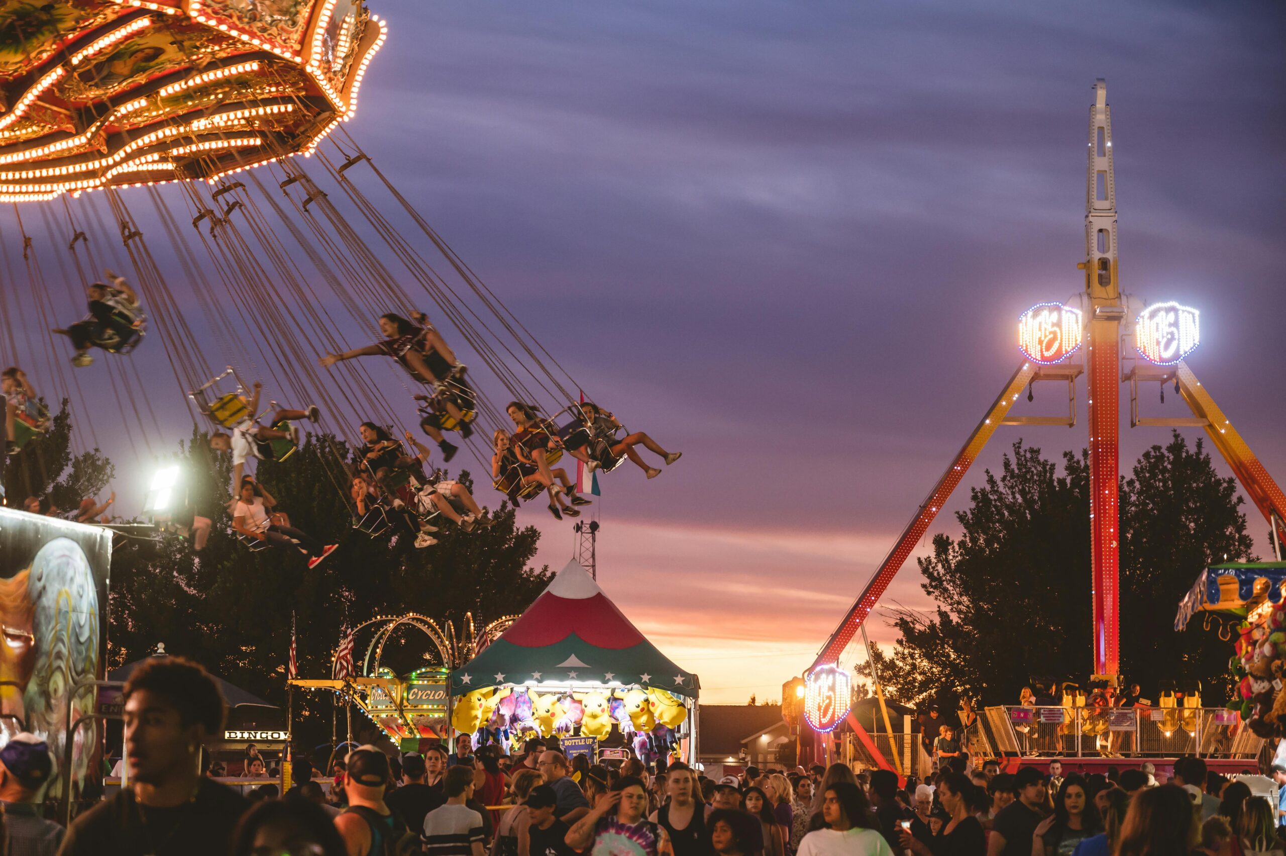 A bustling carnival with thrilling carousel rides under a dramatic sunset sky.