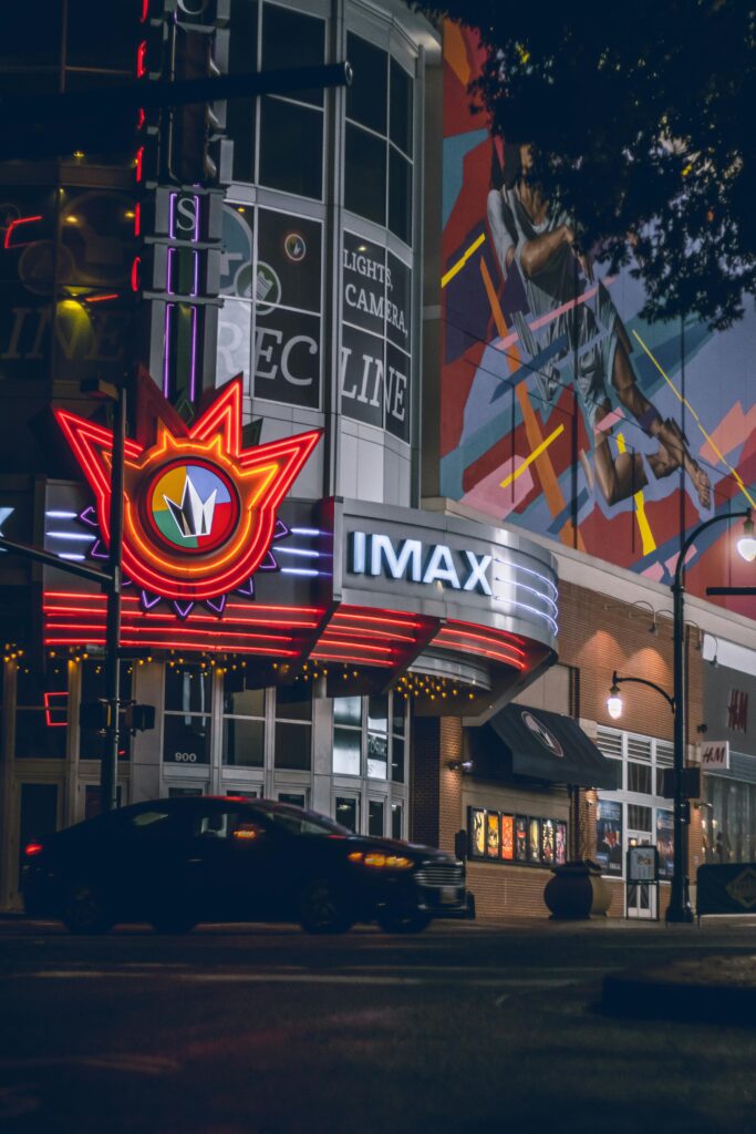 Illuminated neon IMAX theater on an urban street at night, capturing vibrant city life.