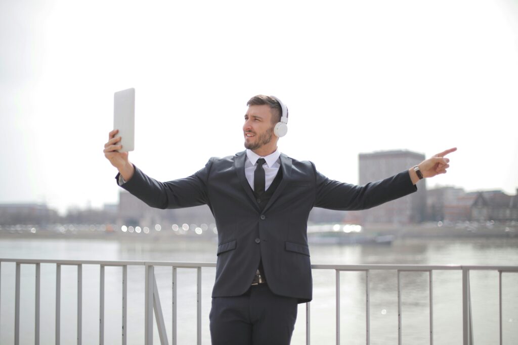 Businessman in formal attire using a tablet for a video call while standing by a river.