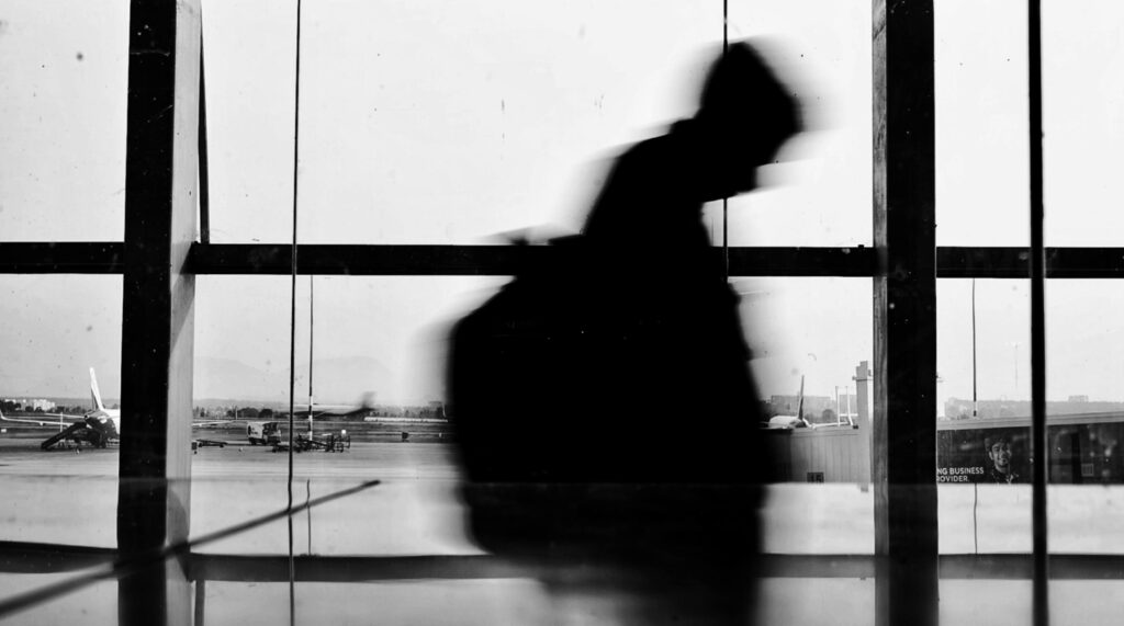 Silhouette of a person walking in an airport terminal with planes visible outside.