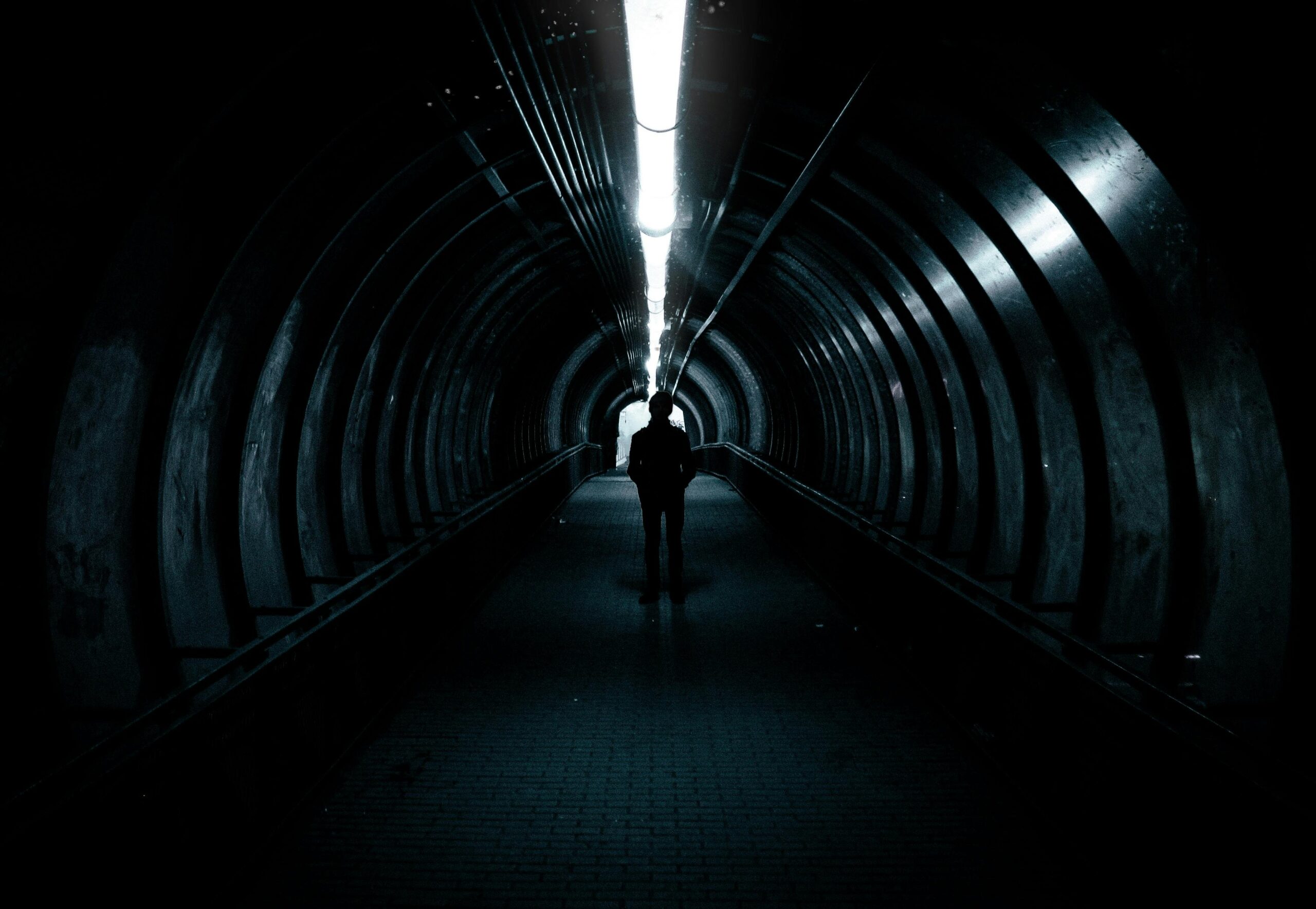 A lone figure stands in a dimly lit tunnel, creating an air of mystery.