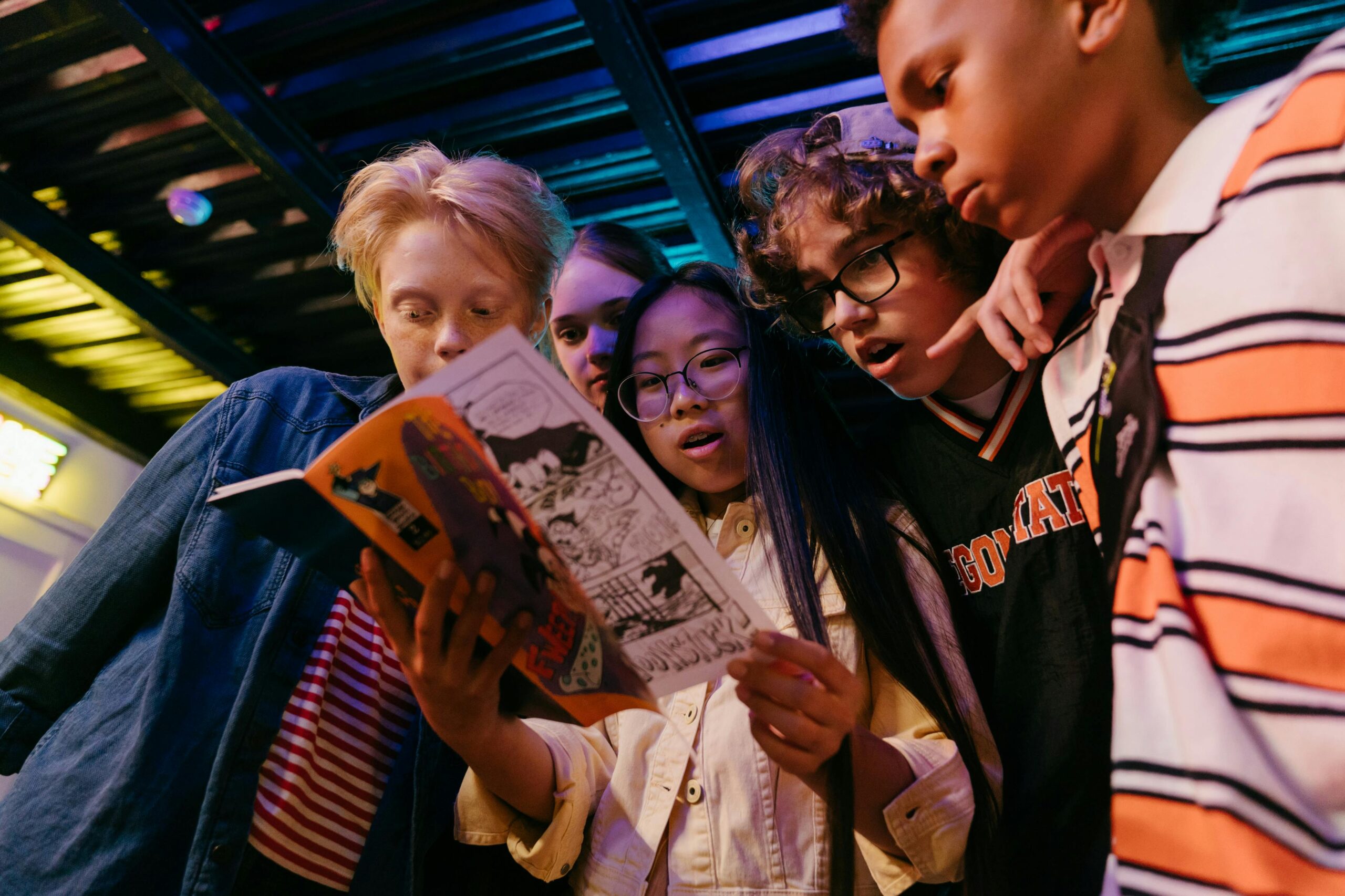 Group of diverse teenagers reading a comic book indoors, showcasing friendship and excitement.