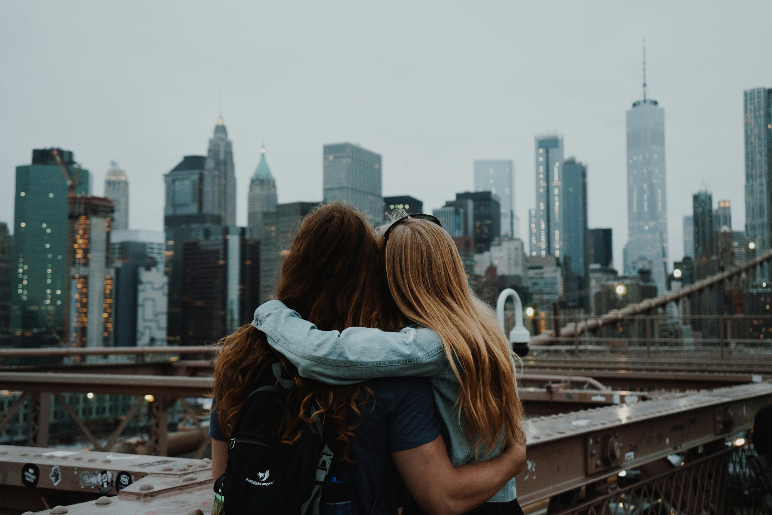 A couple embraces on the Brooklyn Bridge with the New York City skyline in the background.