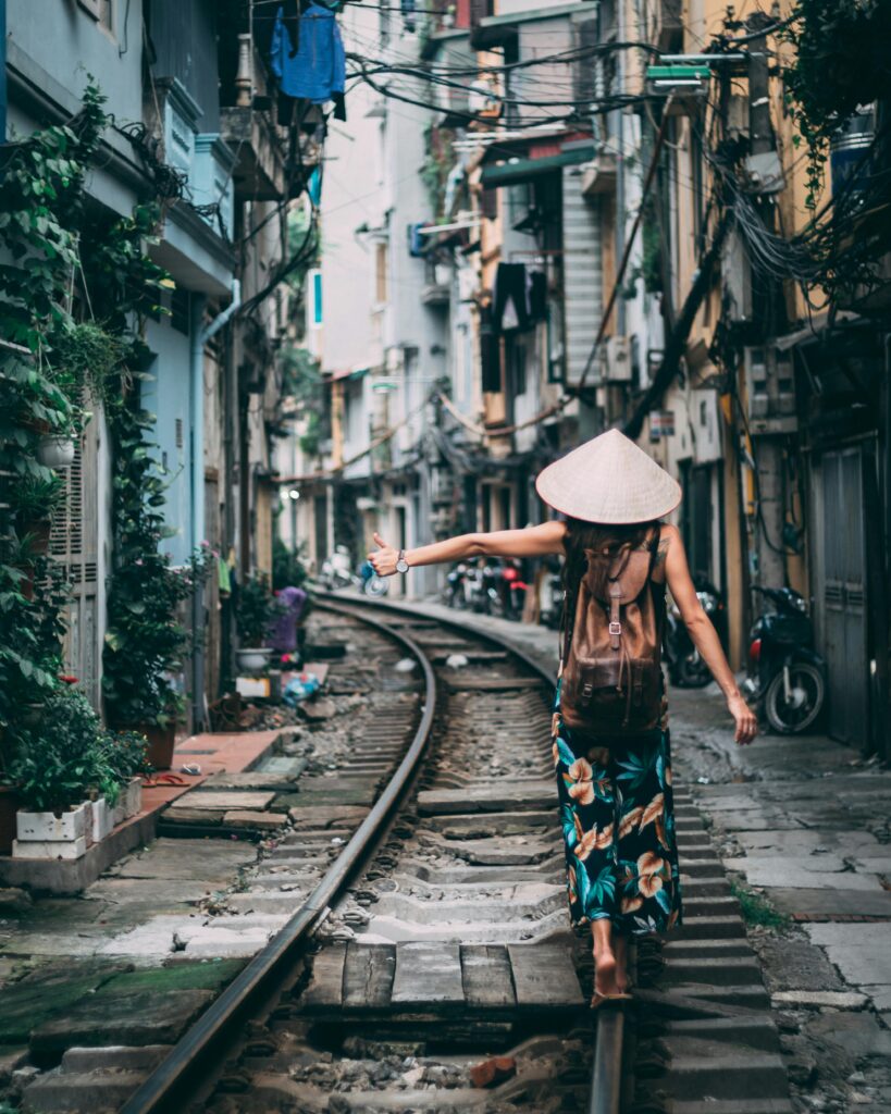 Woman in a conical hat walking on urban train tracks in Vietnam.