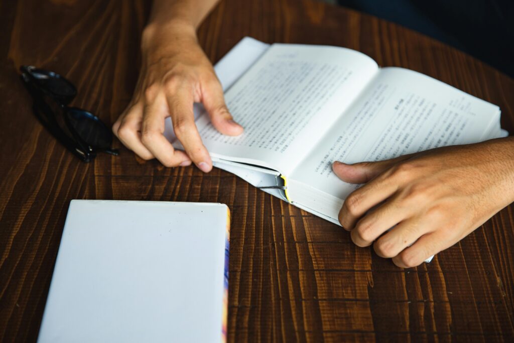 From above crop anonymous bookworm male reading book in hardcover while sitting at wooden round table