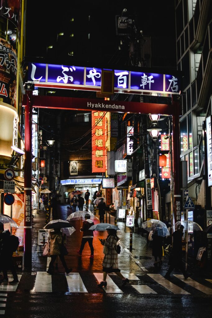 A busy street scene in Shibuya, Japan featuring people with umbrellas walking at night.