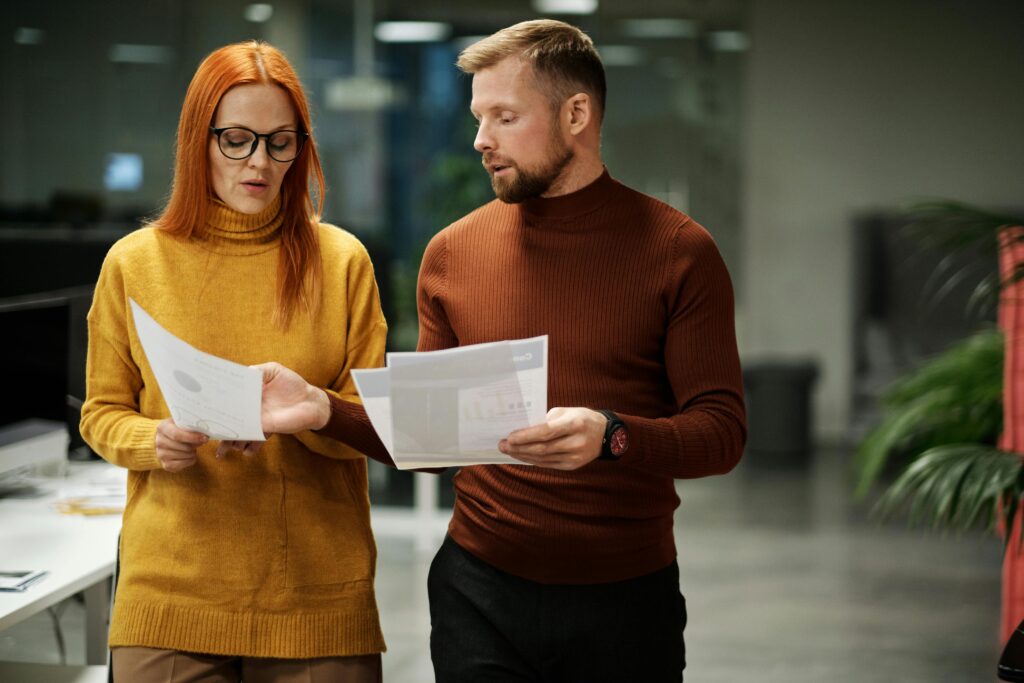 Two professionals in modern office discussing documents, reflecting collaboration and teamwork.