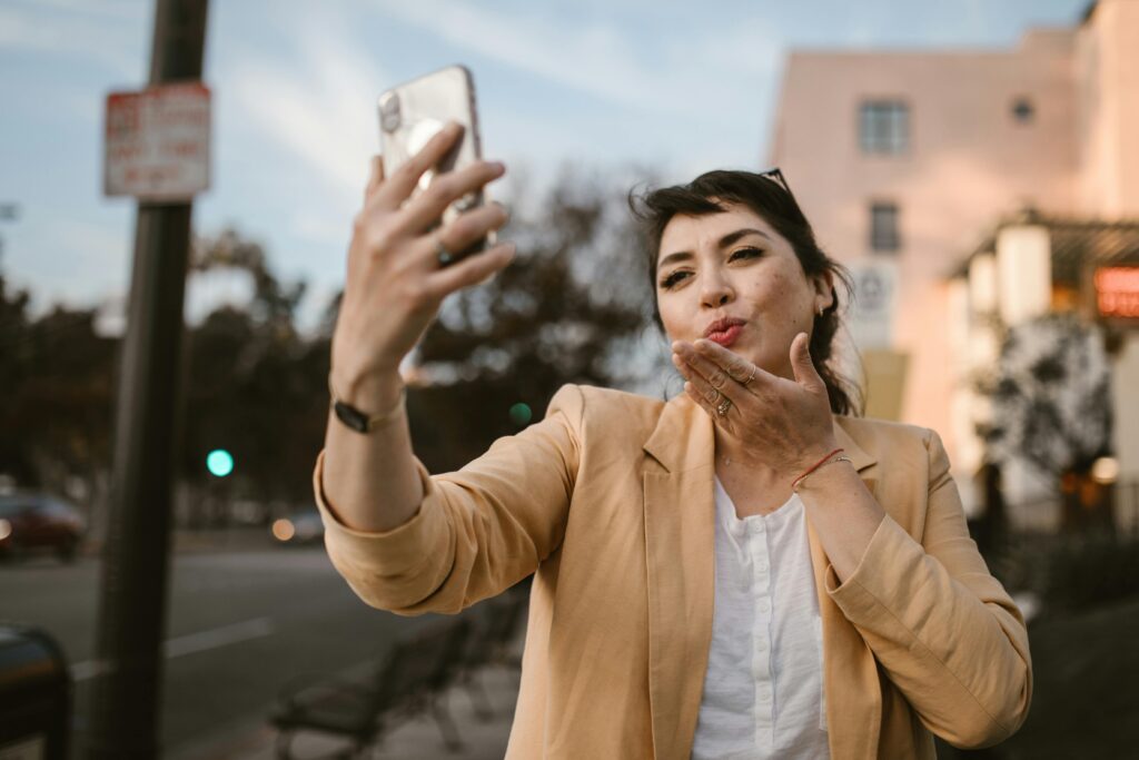 Woman in a casual outfit taking a selfie on a sunny city street.