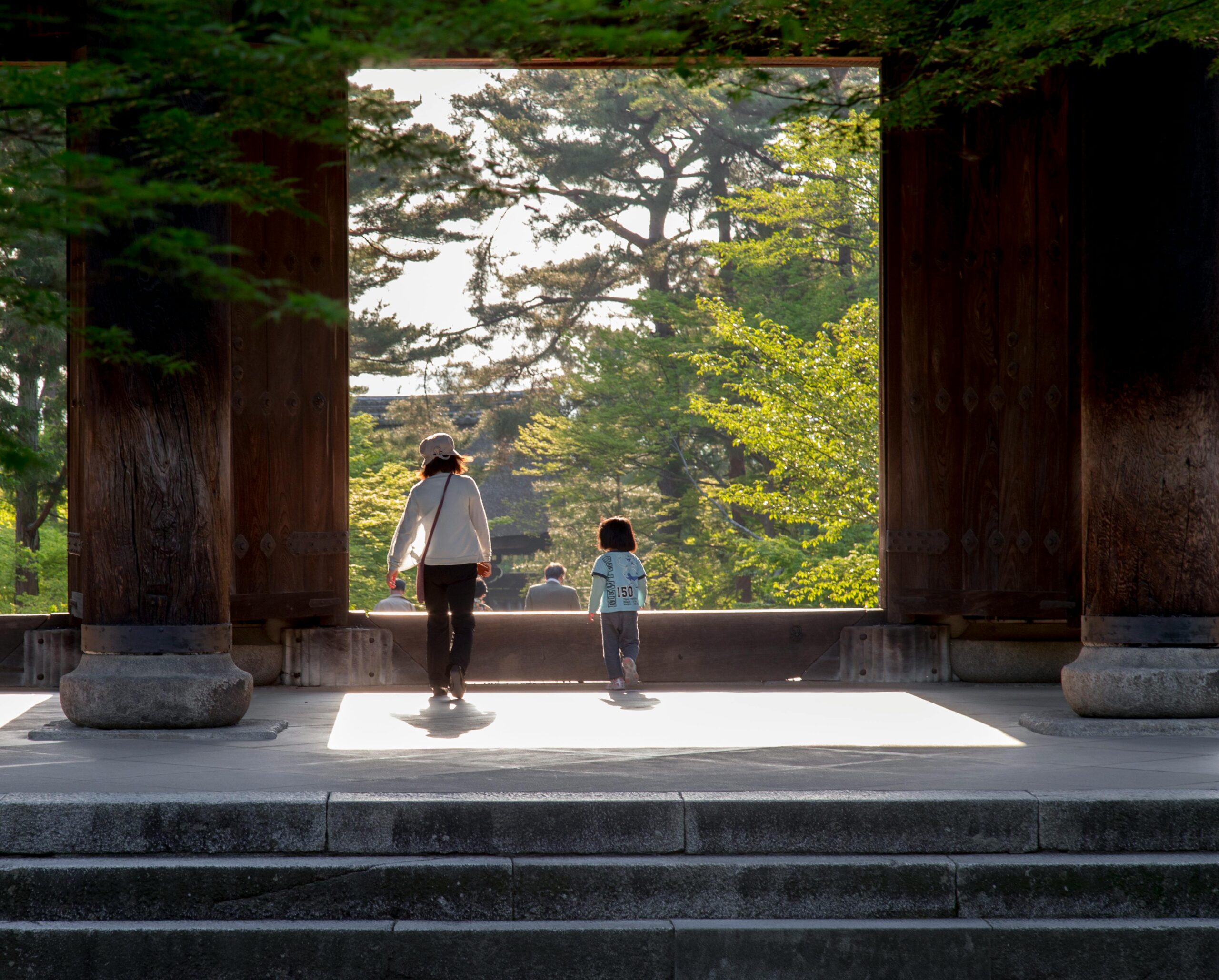 A family strolls through a temple gate surrounded by lush greenery in Kyoto, Japan.