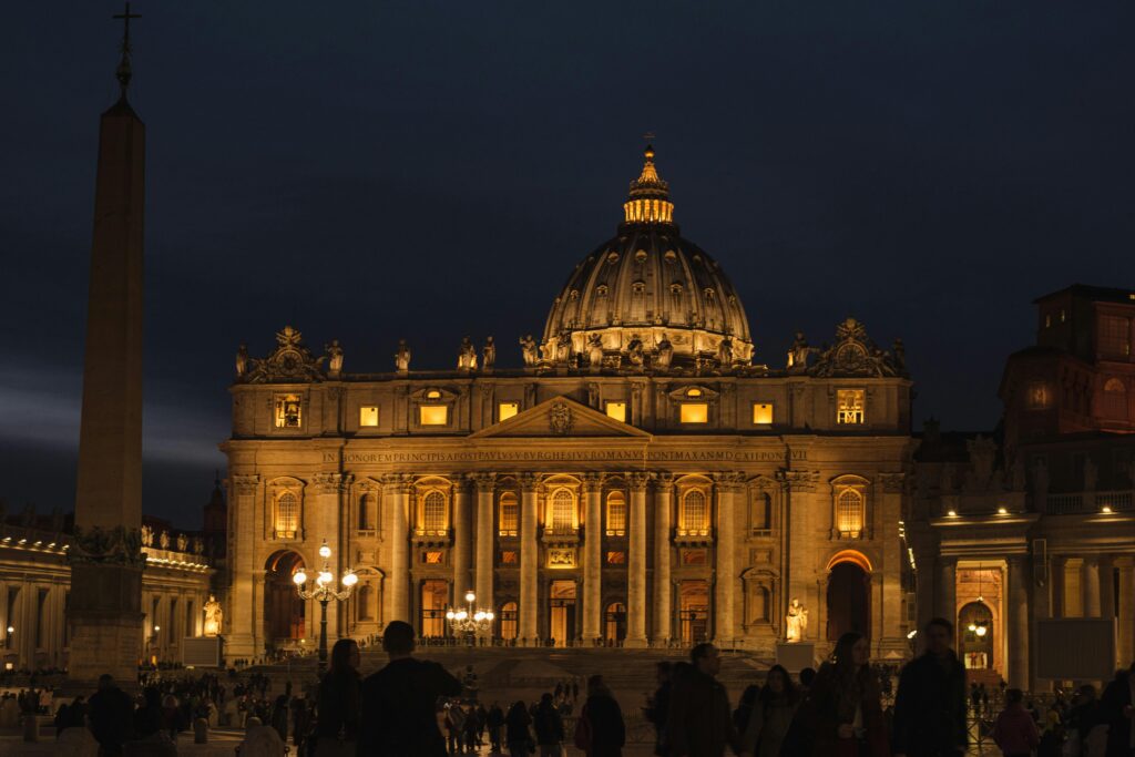 Old stone church with sculptures and columns against anonymous people at dusk in Vatican City Italy