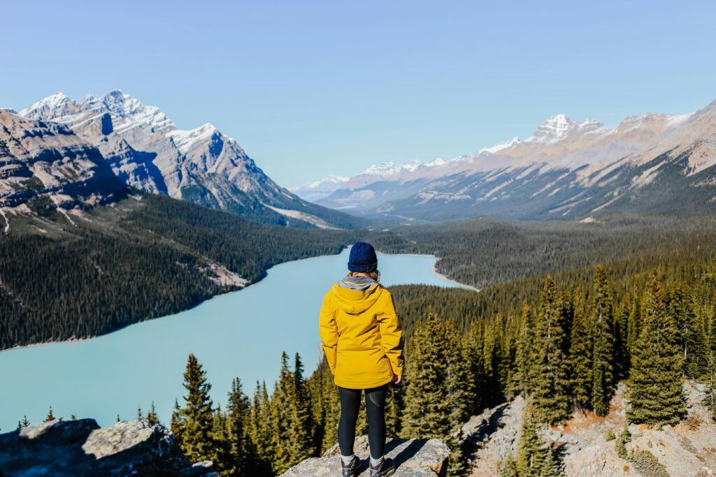 Traveler enjoying breathtaking view of a mountain lake from a rocky cliff in fall.