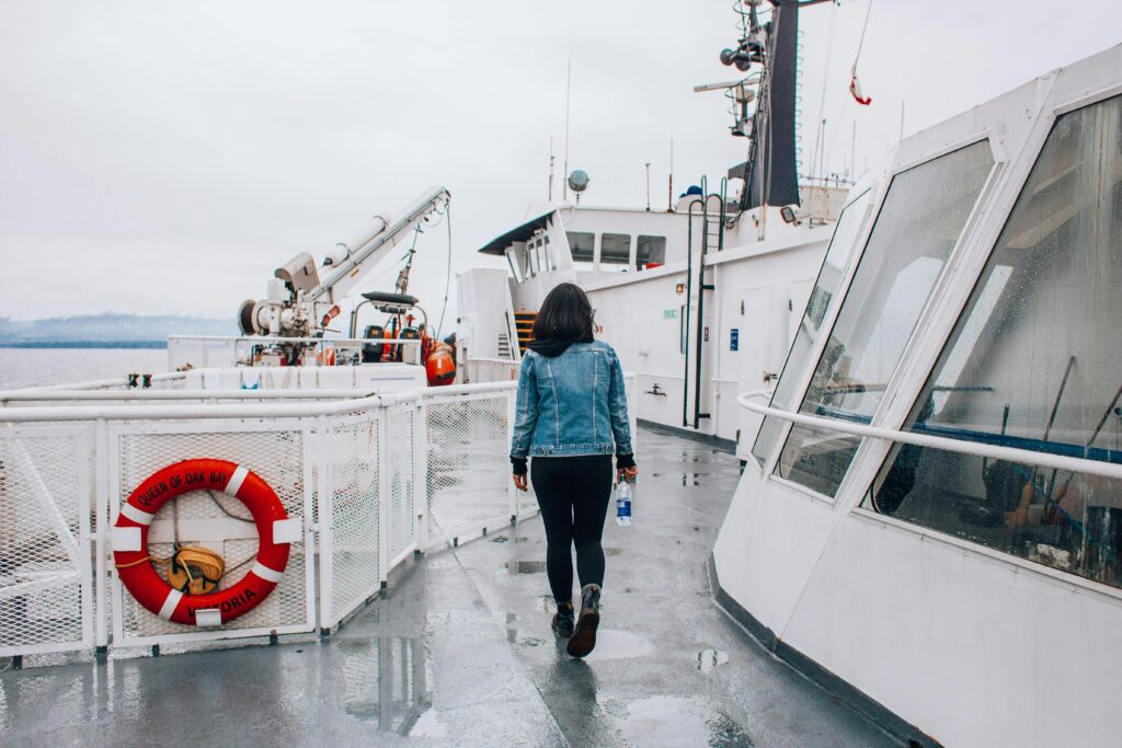 Woman in denim jacket walking on a ferry deck, holding a water bottle, on a cloudy day.