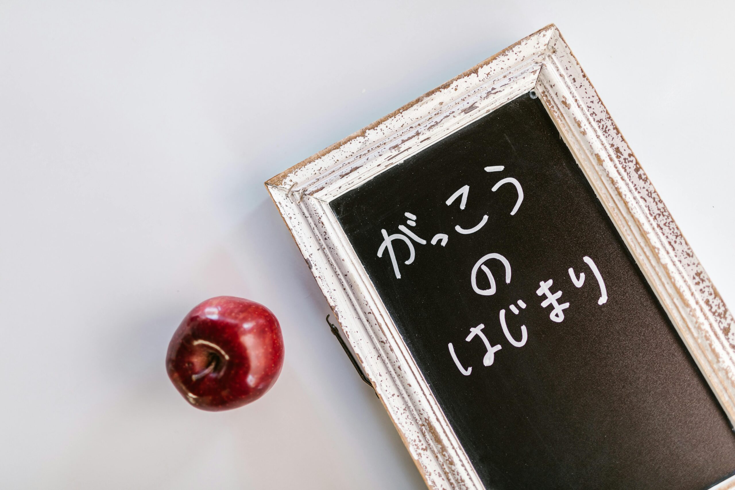 Vintage blackboard with Japanese writing next to a red apple, evoking nostalgic school themes.