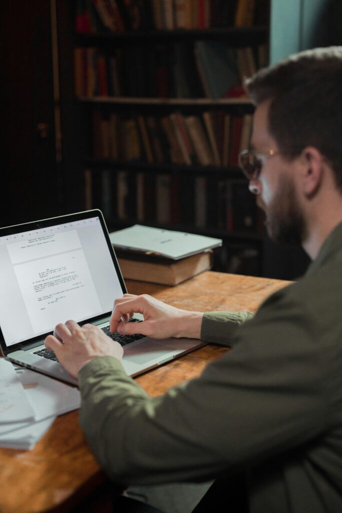 A man typing on a laptop, working in a cozy library setting. Ideal for themes of writing or creativity.