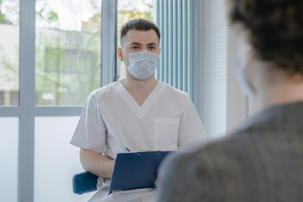 Medical professional in scrubs consulting with a patient while taking notes.