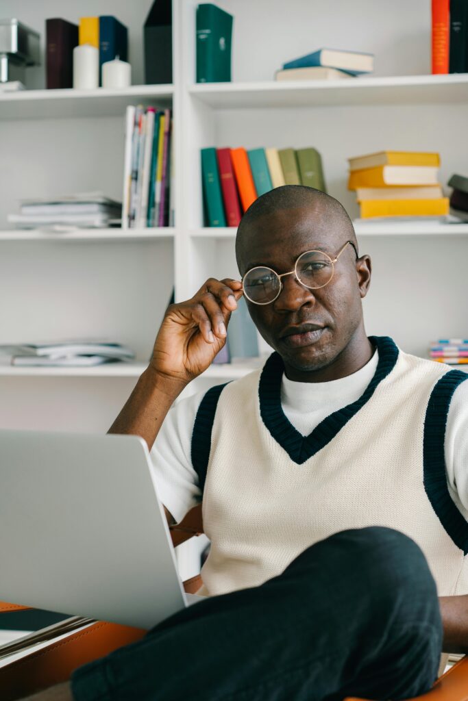 Confident man with glasses using laptop in a modern office with bookshelves.