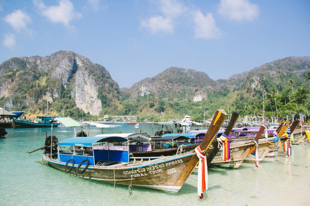 Colorful longtail boats docked by tropical mountains under a clear sky, perfect vacation scene.