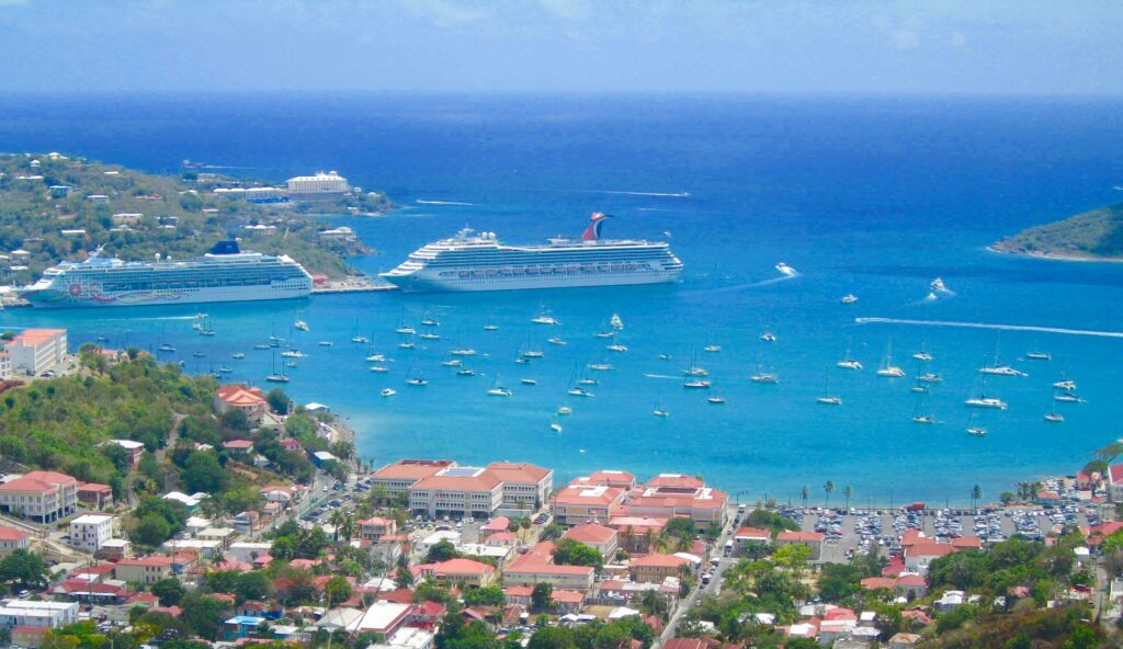 Scenic aerial view of a tropical harbor with cruise ships and sailboats in clear blue waters.