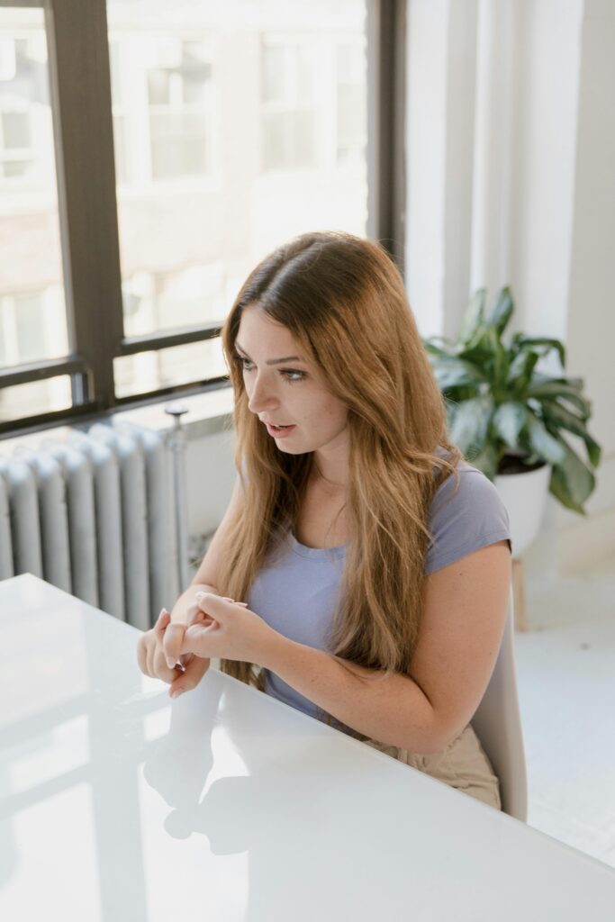 Woman with long hair sitting and using sign language at a table indoors.