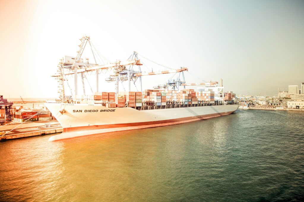Container ship "San Diego Bridge" docked at a bustling harbor during sunset.