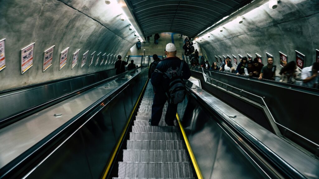 A crowded subway station escalator filled with diverse commuters descending.