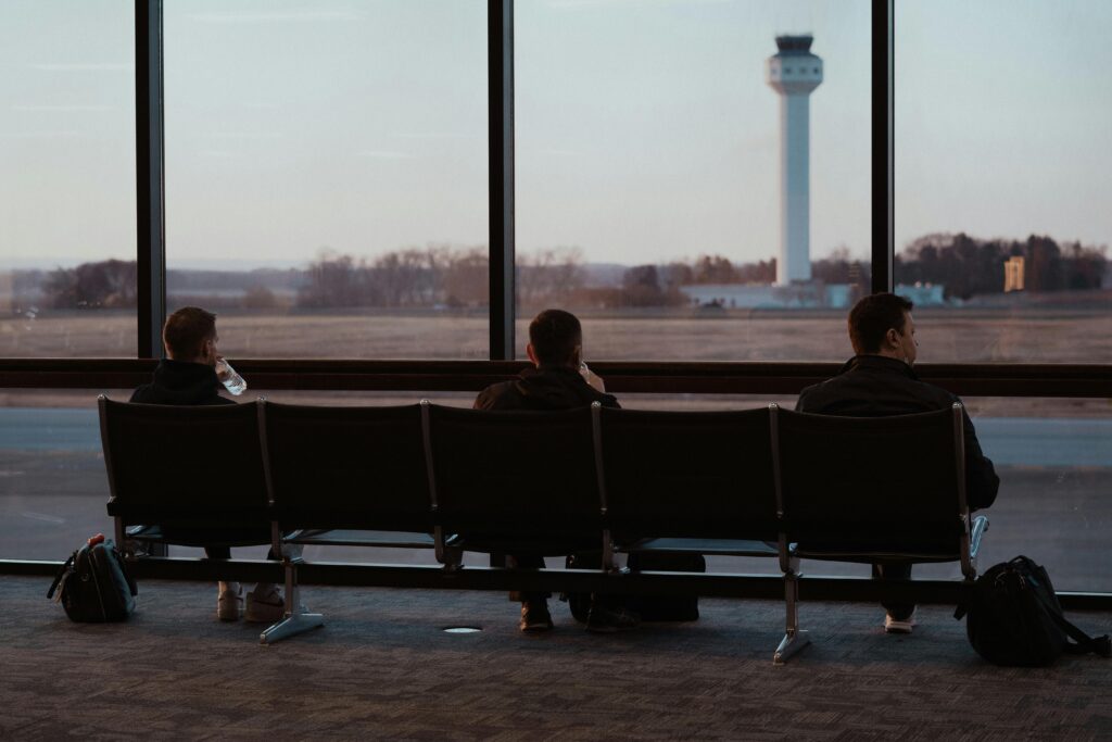 People sitting in airport terminal, watching runway scenes through large windows.