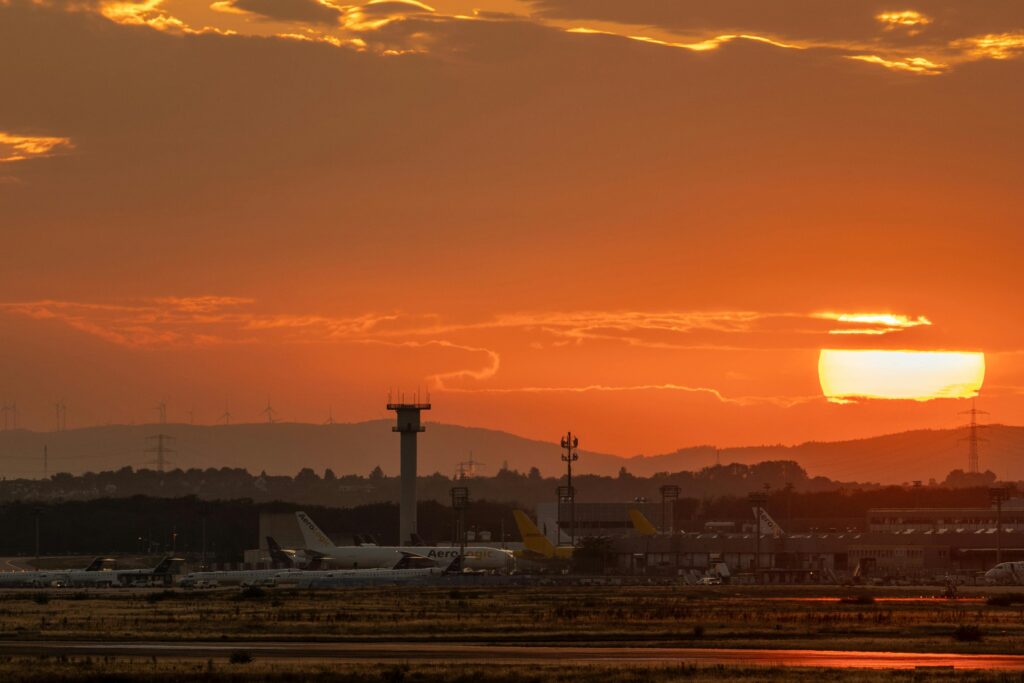 Airplanes parked at the airport with a vibrant sunset backdrop and control tower.