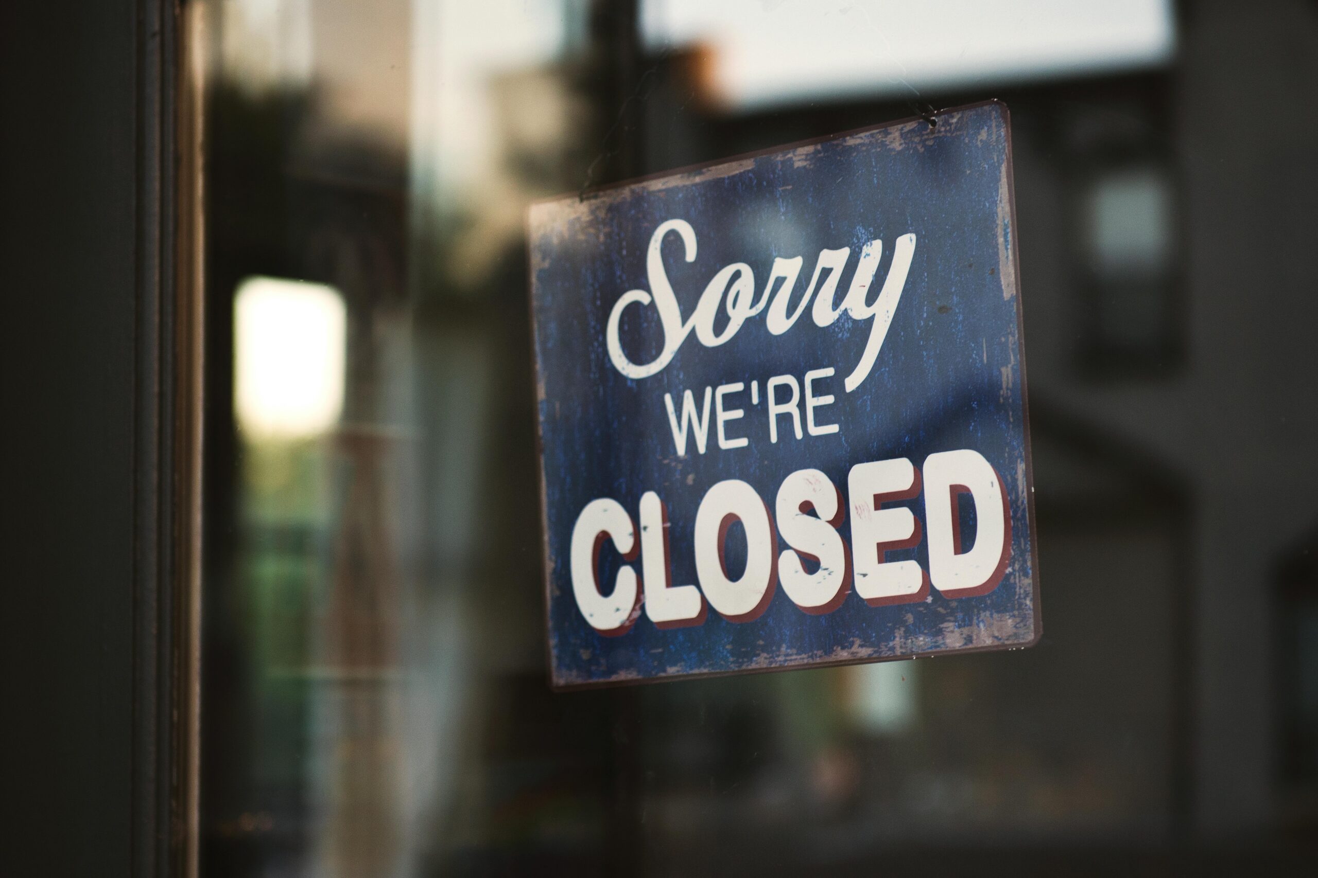 A vintage "Sorry We're Closed" sign on a glass door reflects street view outside.