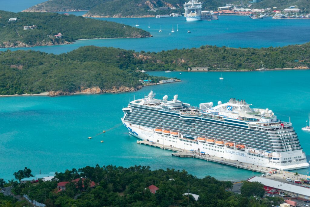 Aerial view of a luxury cruise ship docked in a turquoise Caribbean harbor on a sunny day.