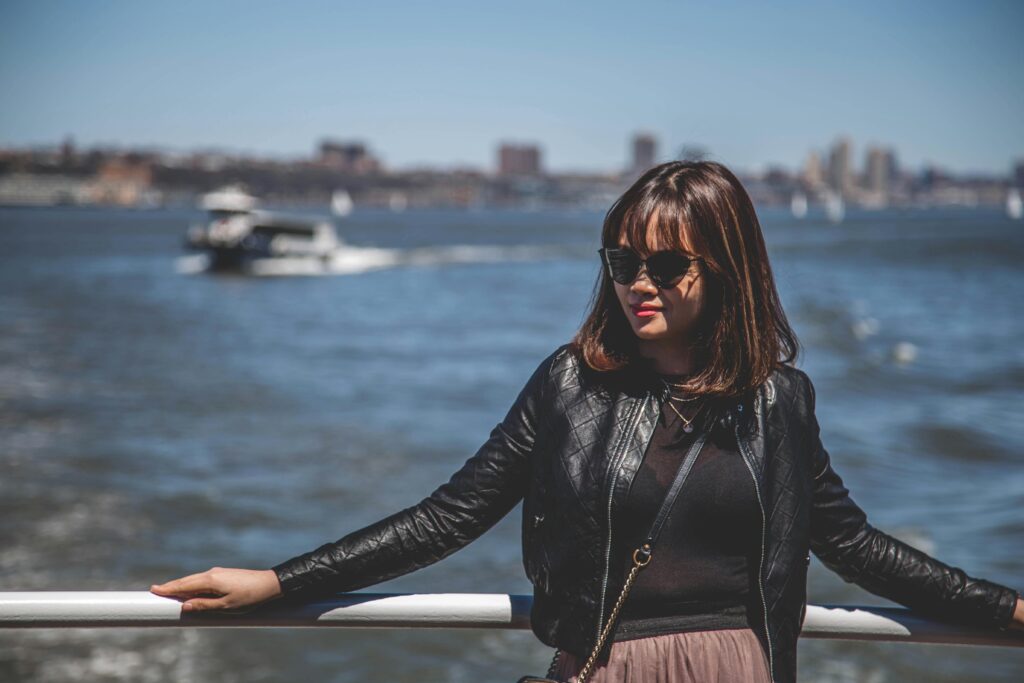 Woman in sunglasses posing effortlessly by a sunny riverfront, exuding chic style.