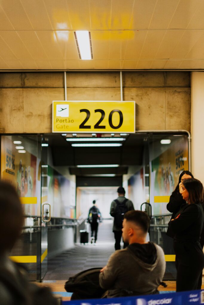 Travelers waiting at a bustling airport gate with a focus on the entrance and sign.