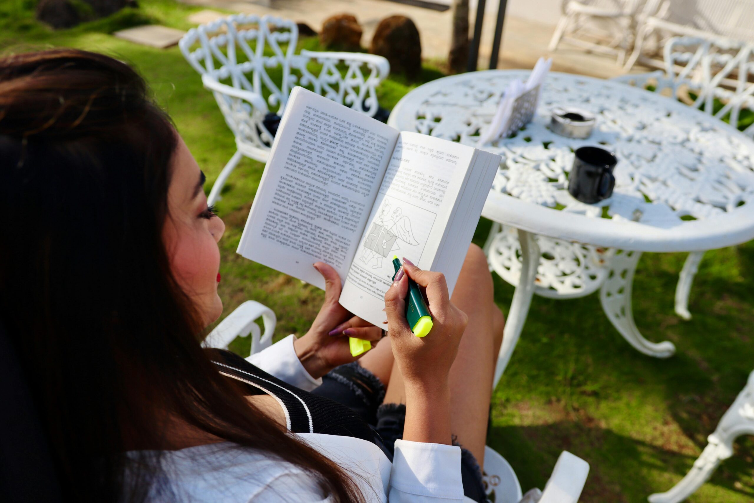 Woman reading in a garden setting with coffee, enjoying leisure time.