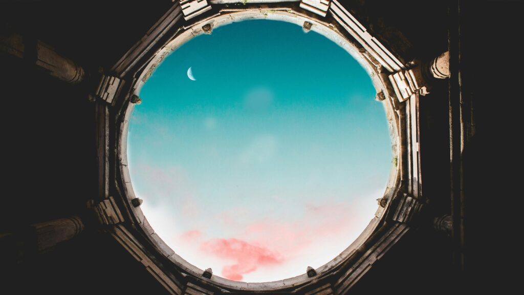 Majestic crescent moon visible through an ancient round oculus against a vibrant sky.