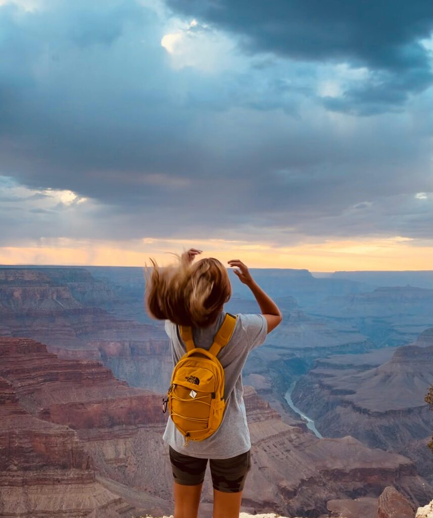 A woman with a backpack enjoying the breathtaking view of the Grand Canyon at sunset.