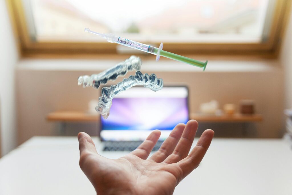 A syringe and dental aligner float above a hand in a modern office, signifying advanced dental care technology.