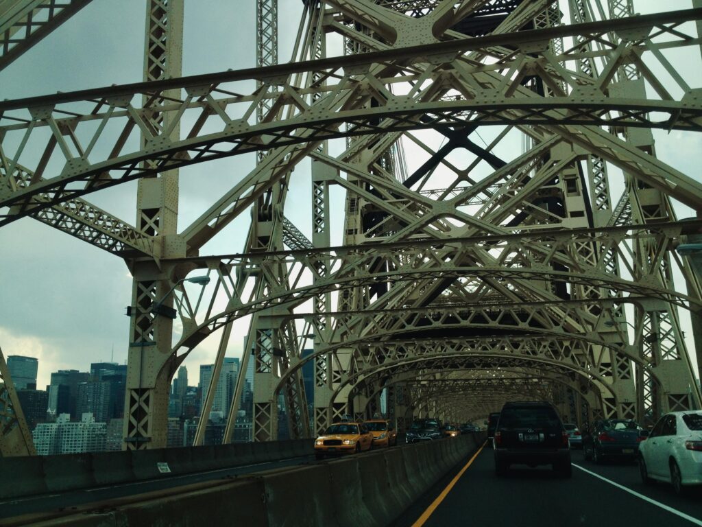 View of Queensboro Bridge's metal lattice structure with cityscape visible.