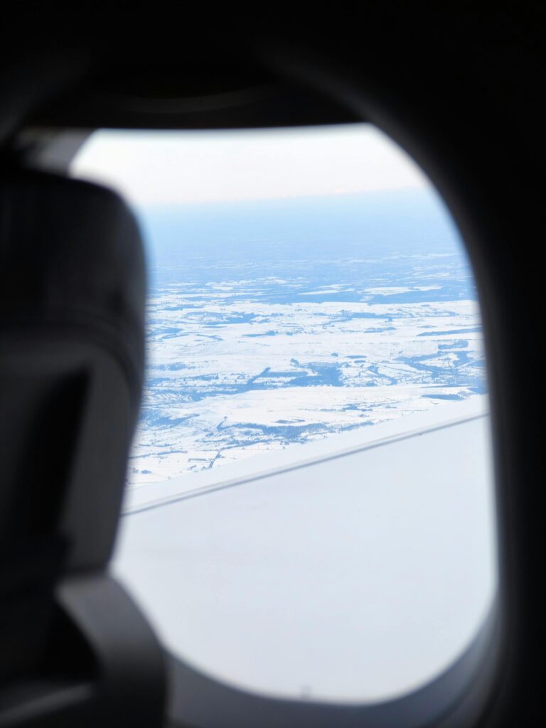 Aerial view of a snow-covered landscape seen through an airplane window, capturing serene winter beauty.