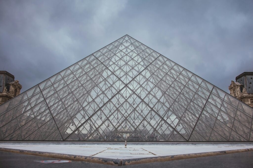 The Louvre Pyramid stands majestically in Paris, showcasing modern architecture against a cloudy sky.