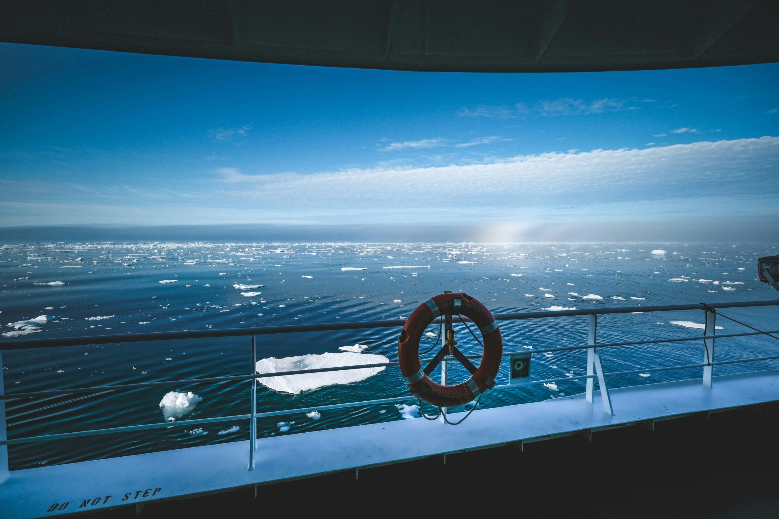 Stunning view of the Arctic Ocean with icebergs seen from a ship's deck under a clear blue sky.