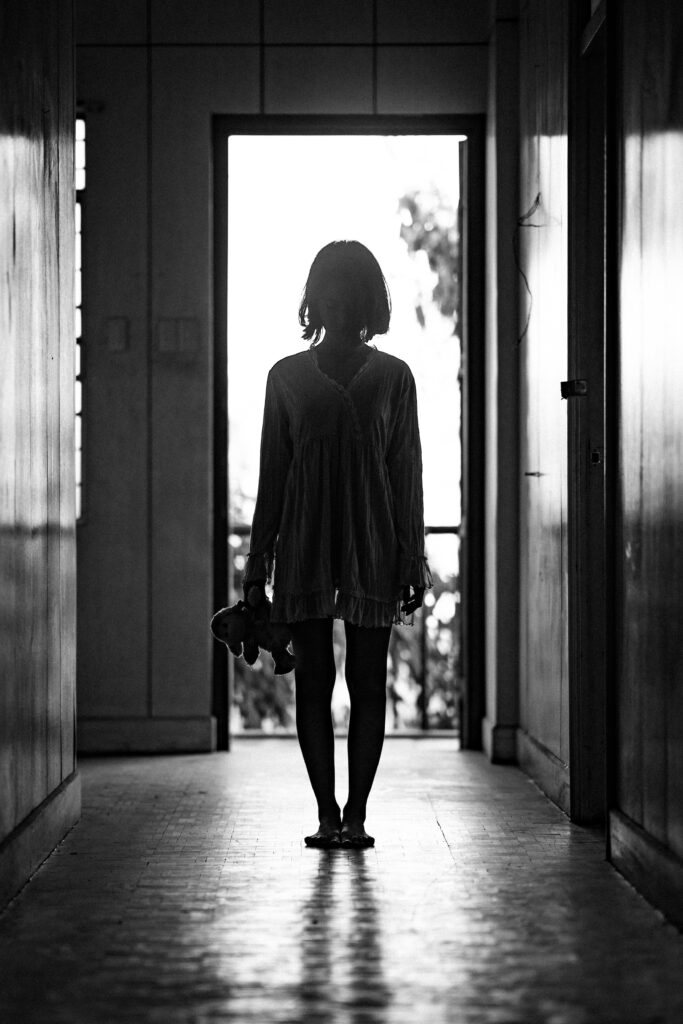 Moody black and white silhouette of a woman standing in a hallway, evoking mystery and contemplation.