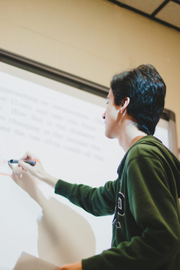 A student writing on a whiteboard indoors, capturing an educational moment.